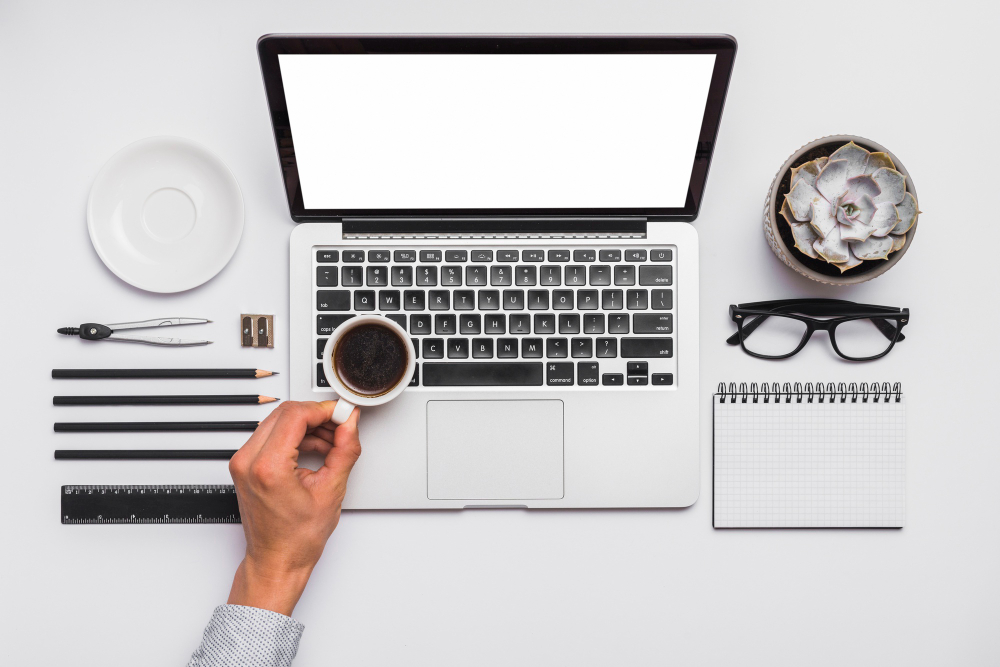 a person s hand holding cup of black coffee over the laptop on office desk